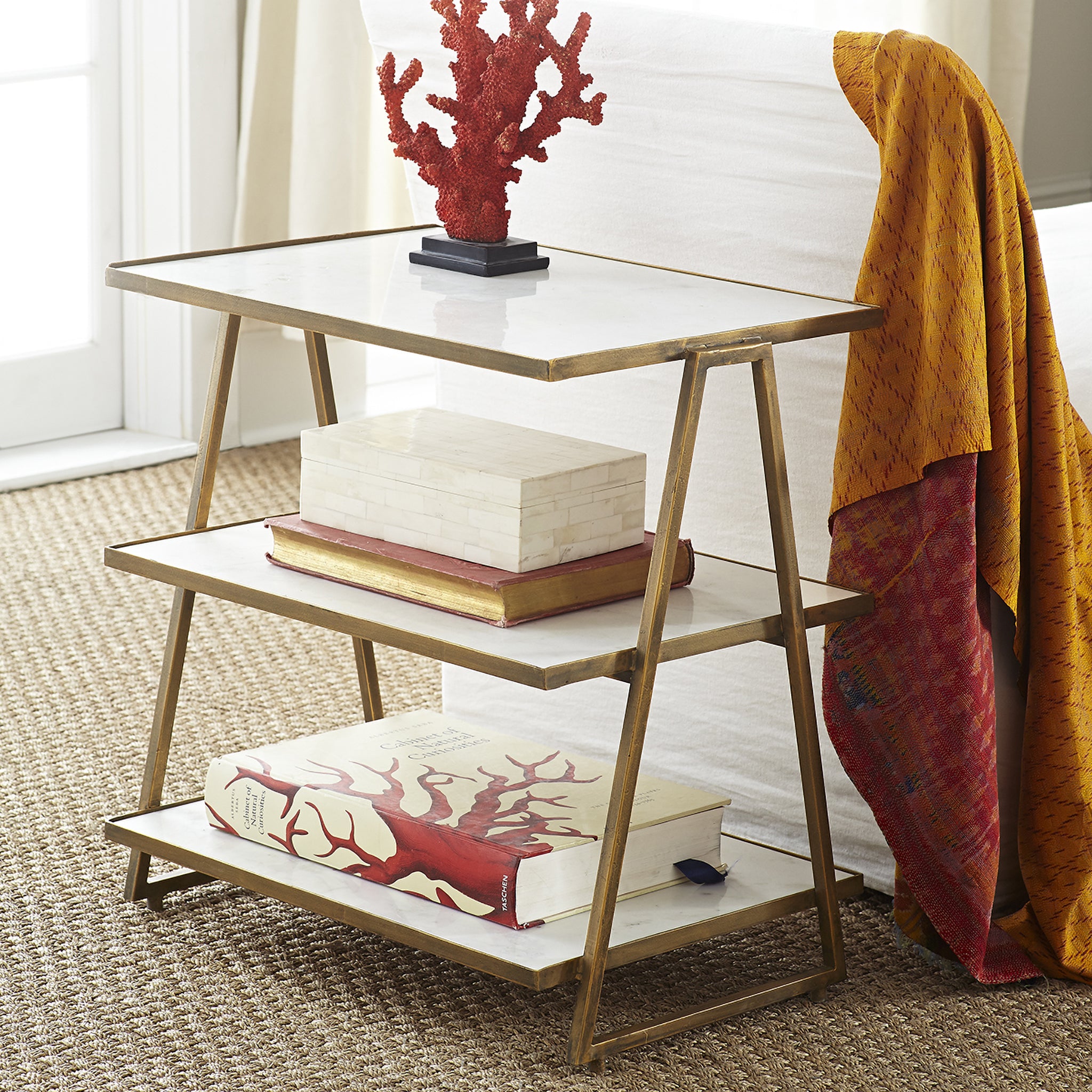 Three Tier Marble Top Table - angled shot, warm lighting in a living space, books and red coral.