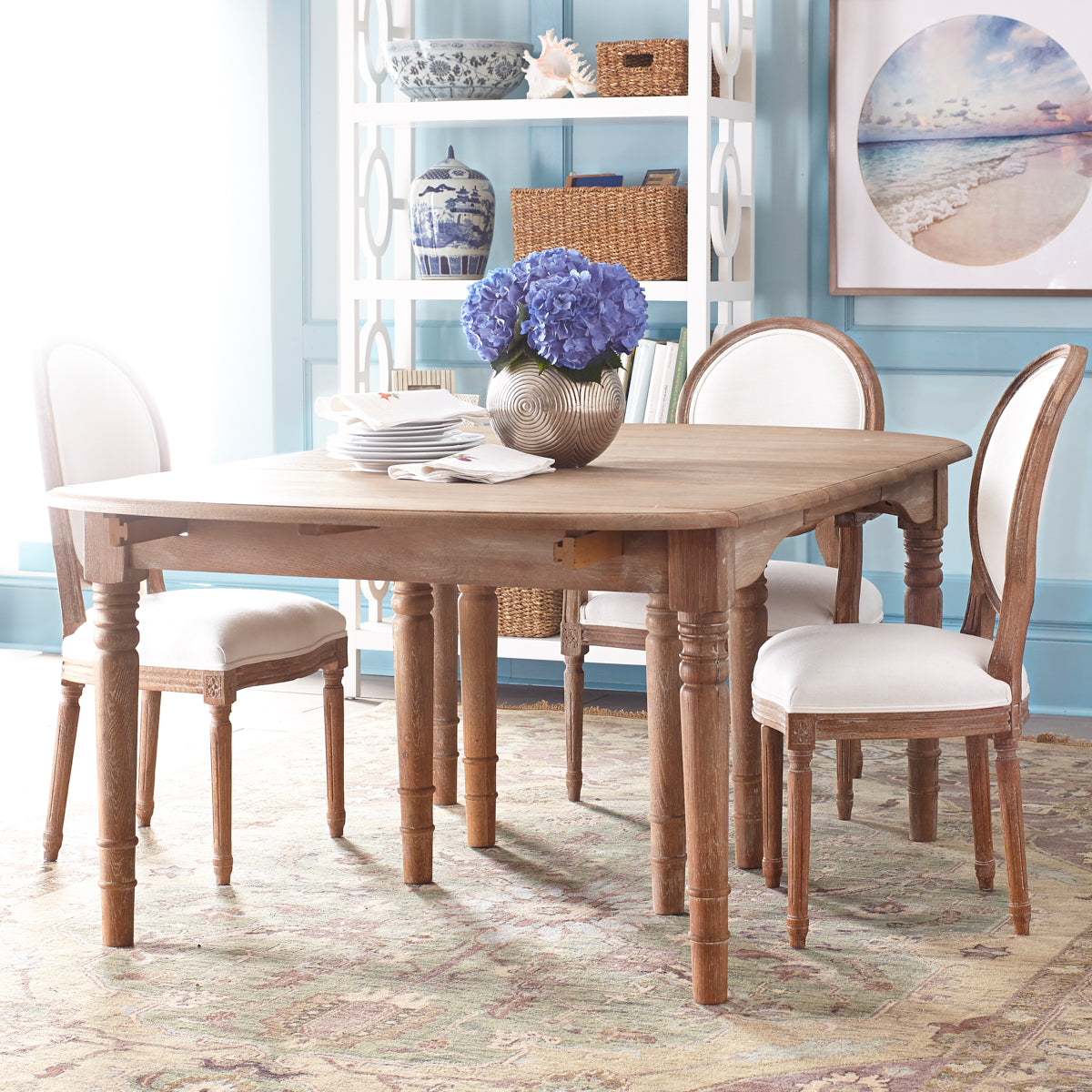 Expandable Oak Farmhouse Table – Styled in a dining room, set with blue hydrangeas, white chairs.