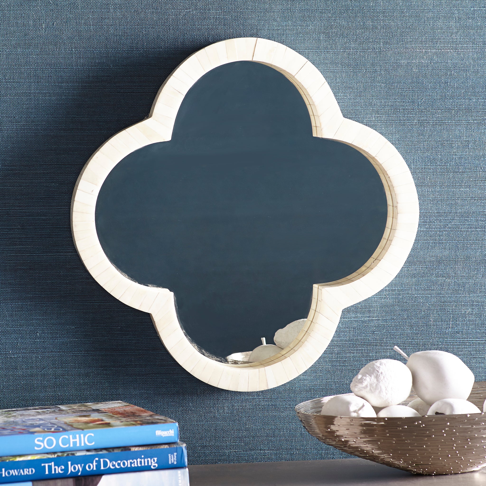 Clover Bone Mirror – mounted on blue wall, tabletop decor foreground.